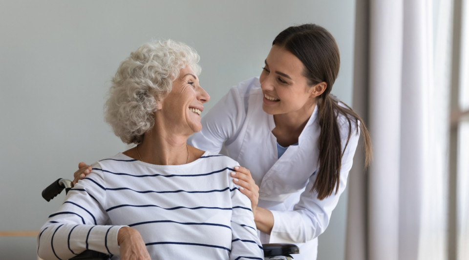 técnica sociosanitaria sonriendo a una anciana en silla de ruedas